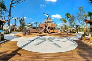 A playground with a slide and play structures, surrounded by palm trees and a clear sky.
