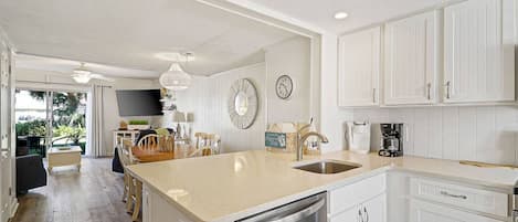 A modern kitchen with white cabinetry, a stainless steel dishwasher, and a dining area with a wooden table and chairs.
