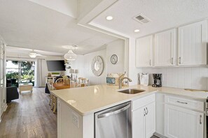 A modern kitchen with white cabinetry, a stainless steel dishwasher, and a dining area with a wooden table and chairs. - Dog- Friendly Villa- Walk to the Beach (Hilton Head Island)
