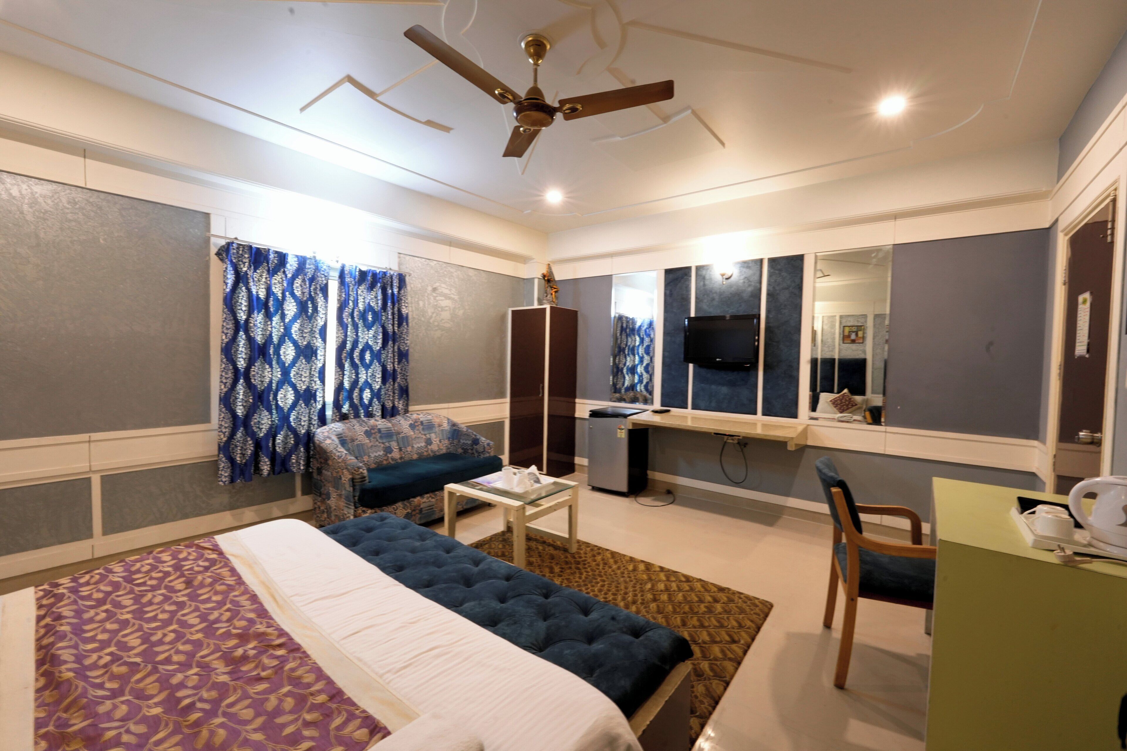 A bedroom with a bed, a desk, a chair, a ceiling fan, and a TV.