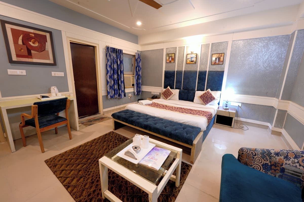 Ein modernes Hotelzimmer mit Bett, Schreibtisch, Sessel, Couchtisch und einem gemusterten Teppich.