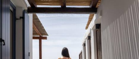 A corridor with a wooden ceiling and white walls, leading to a seating area with a view of the sea.
