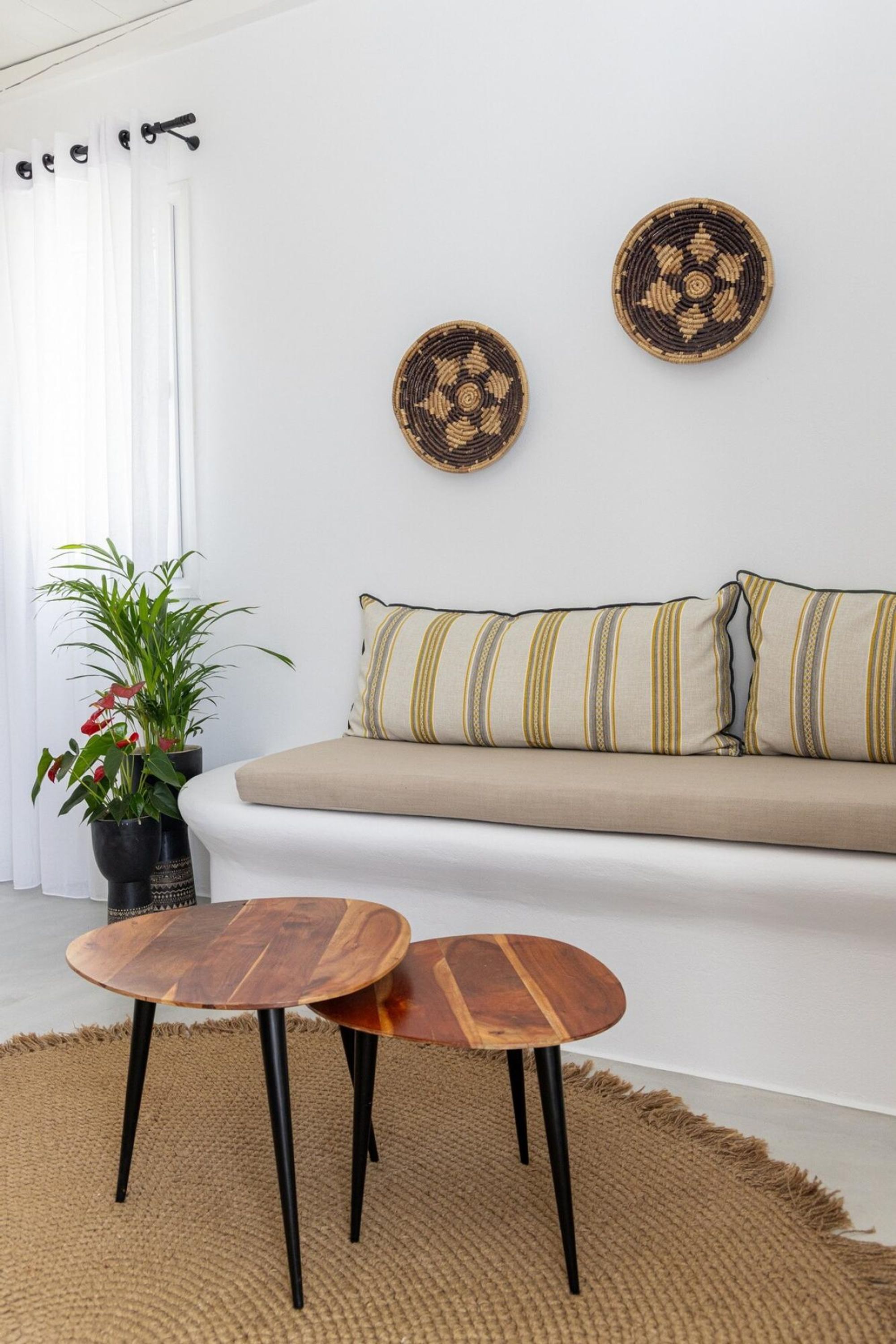 Uma sala de estar moderna com sofá, duas decorações circulares de fibra, almofada listrada, planta em vaso e mesa de centro de madeira.