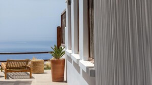 Un balcon avec un fauteuil en osier et un pot de fleurs, offrant une vue sur la côte.