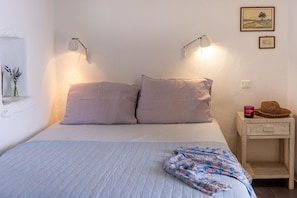 Ein Schlafzimmer mit einem Bett, zwei Nachttischlampen, einem Nachttisch mit Kerze und Hut sowie einer Wand mit einem Gemälde.