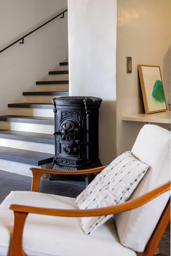 Un intérieur moderne avec un poêle à bois noir, une chaise blanche agrémentée d’un coussin à motifs et un escalier.