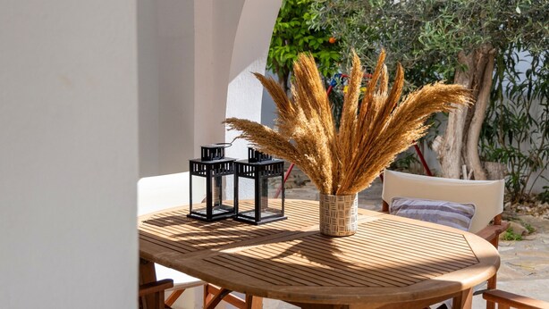 A round wooden table with a woven basket containing pampas grass, two black lanterns, and a cushion on a white chair. - Cycladic Vibes Tinos (Tinos)