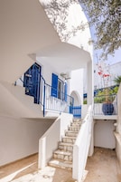 Um edifício branco com uma escadaria e guarda-corpo azuis, que levam a uma porta com uma persiana azul.