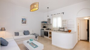 A modern living room with a white sofa, a coffee table, and a kitchen area with a white countertop and cabinets. - Cycladic Vibes Tinos (Tinos)