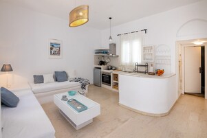 Una sala de estar moderna con un sofá blanco, una mesa de centro y una cocina con encimera y armarios blancos.