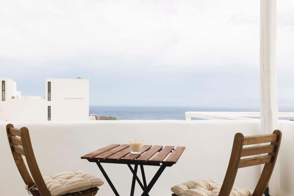 Un balcon avec une table en bois et deux chaises, offrant une vue sur la côte.