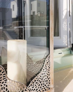 A modern interior with a glass partition, a white candle, and a geometric metal bench. - Ballos for 4 in Exomvourgo (Tinos)