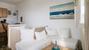 A white sofa with cushions, a wooden coffee table, and a painting of the ocean on the wall. - Ballos for 4 in Exomvourgo (Tinos)