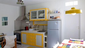 A compact kitchen with yellow cabinets, a white refrigerator, and a dining area with a table and chairs. - Amberi Tinos in Panormos (Tinos)