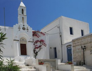 Un edificio blanco con una torre de campanas, una puerta azul y escalones que conducen a la entrada.