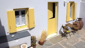 A small outdoor seating area with a table and chairs, a potted plant, and a stone floor. - Amberi Tinos in Panormos (Tinos)