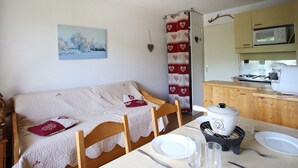 A cozy room with a bed, a dining table set with plates and glasses, a microwave, and a stove. - Cozy studio with balcony and pets allowed in Chamrousse (Chamrousse)