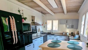 Een moderne keuken met een zwarte koelkast, een magnetron en een fornuis. Er zijn kastjes, een spoelbak en een raam dat voor natuurlijk licht zorgt.