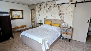Een slaapkamer met een bed, een bankje, een nachtkastje, een spiegel en een kledingkast.