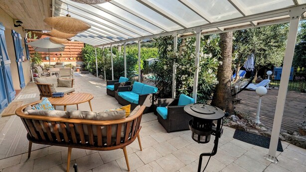 Een buitenterras met rieten meubilair, een ronde tafel en een pergola.
