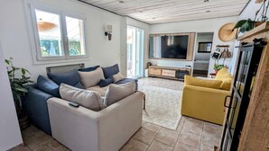 Een ruime woonkamer met een zithoek, een gele fauteuil, een televisie en een groot raam.
