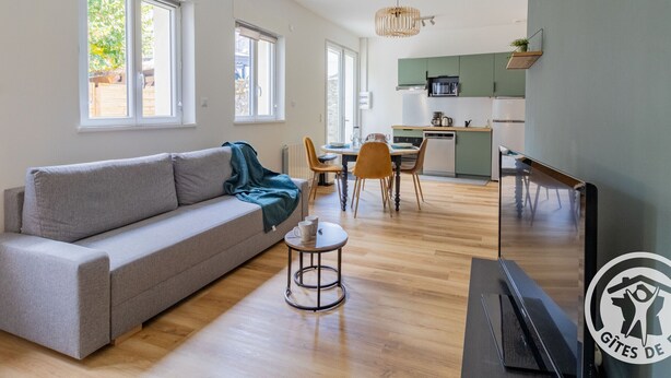 A modern living room with a sofa, coffee table, and dining area with chairs. There is a kitchen in the background with a microwave and a sink. - Renovated house with garden near Angers (Rochefort-sur-Loire)
