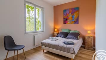A bedroom with a bed, a chair, a window, and a painting on the wall.