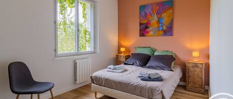 Ein Schlafzimmer mit einem Bett, einem Sessel, einem Fenster und einem Bild an der Wand.