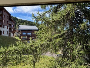 Un edificio a più piani con balconi, circondato da alberi di conifere fitti.