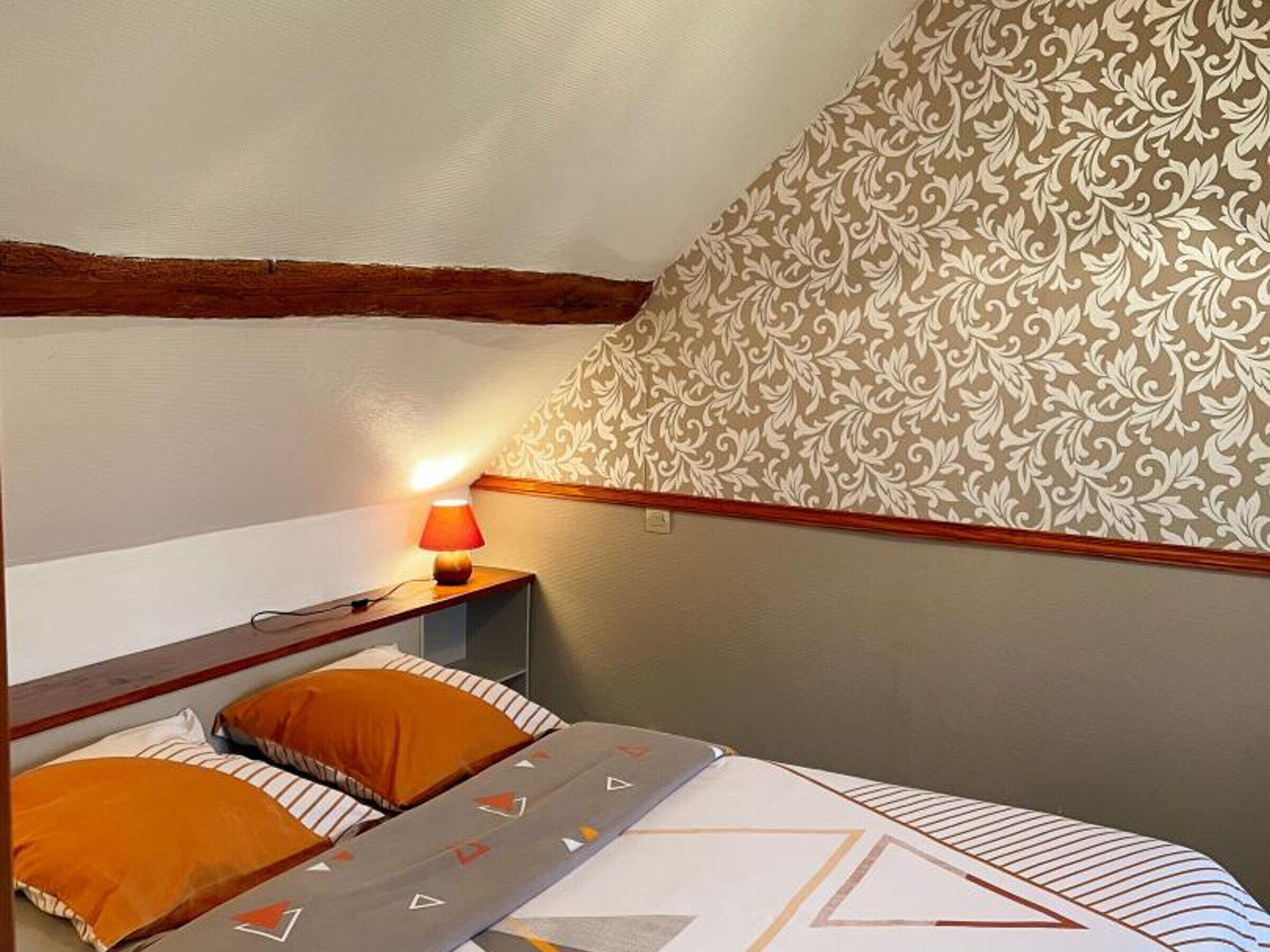 A bedroom with a bed, two pillows, a bedside table with a lamp, and a patterned wall.