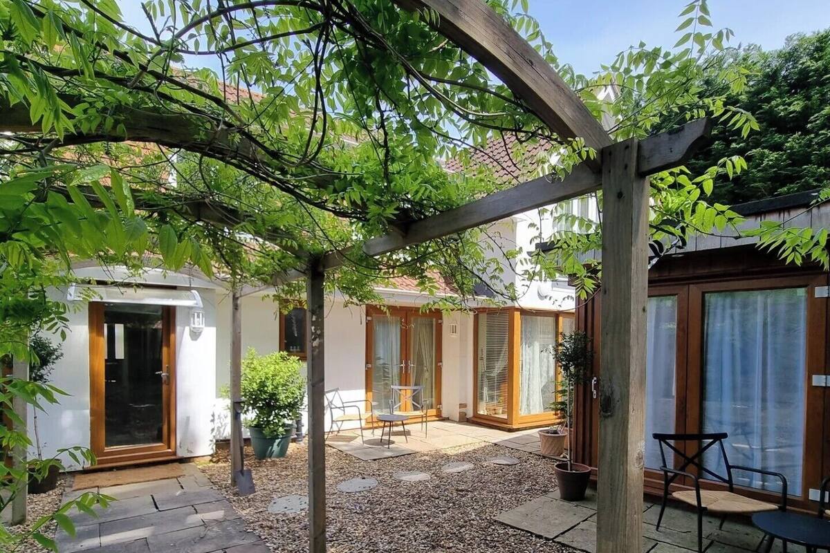 A courtyard with a pergola, stone pathway, seating area, and a building with a glass door.