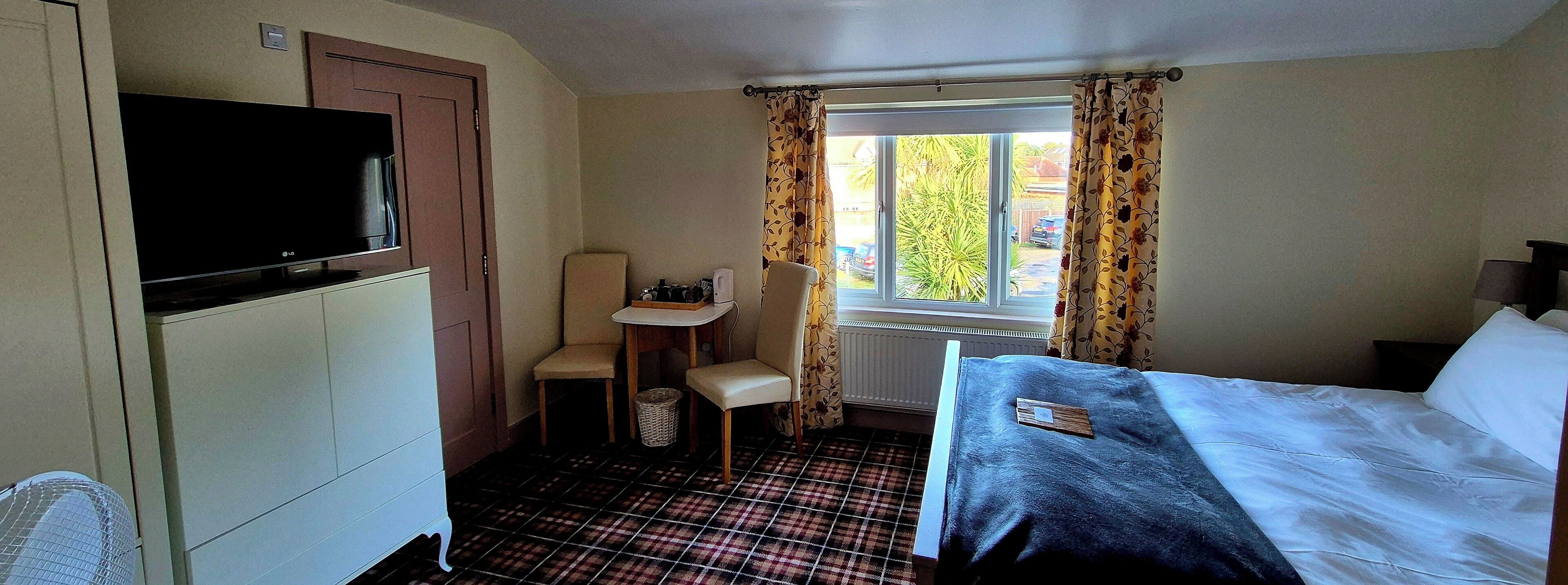 A hotel room with a bed, a TV, a chair, a small table, and a window with curtains.