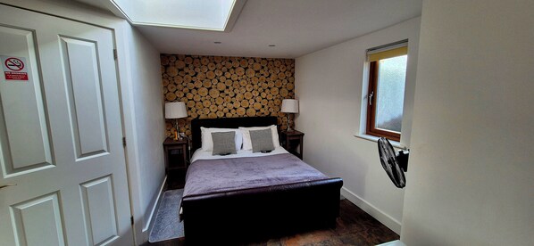 Une chambre d’hôtel étroite, avec un lit, deux lampes de chevet, une fenêtre avec un store et un panneau « Interdiction de fumer » sur la porte.