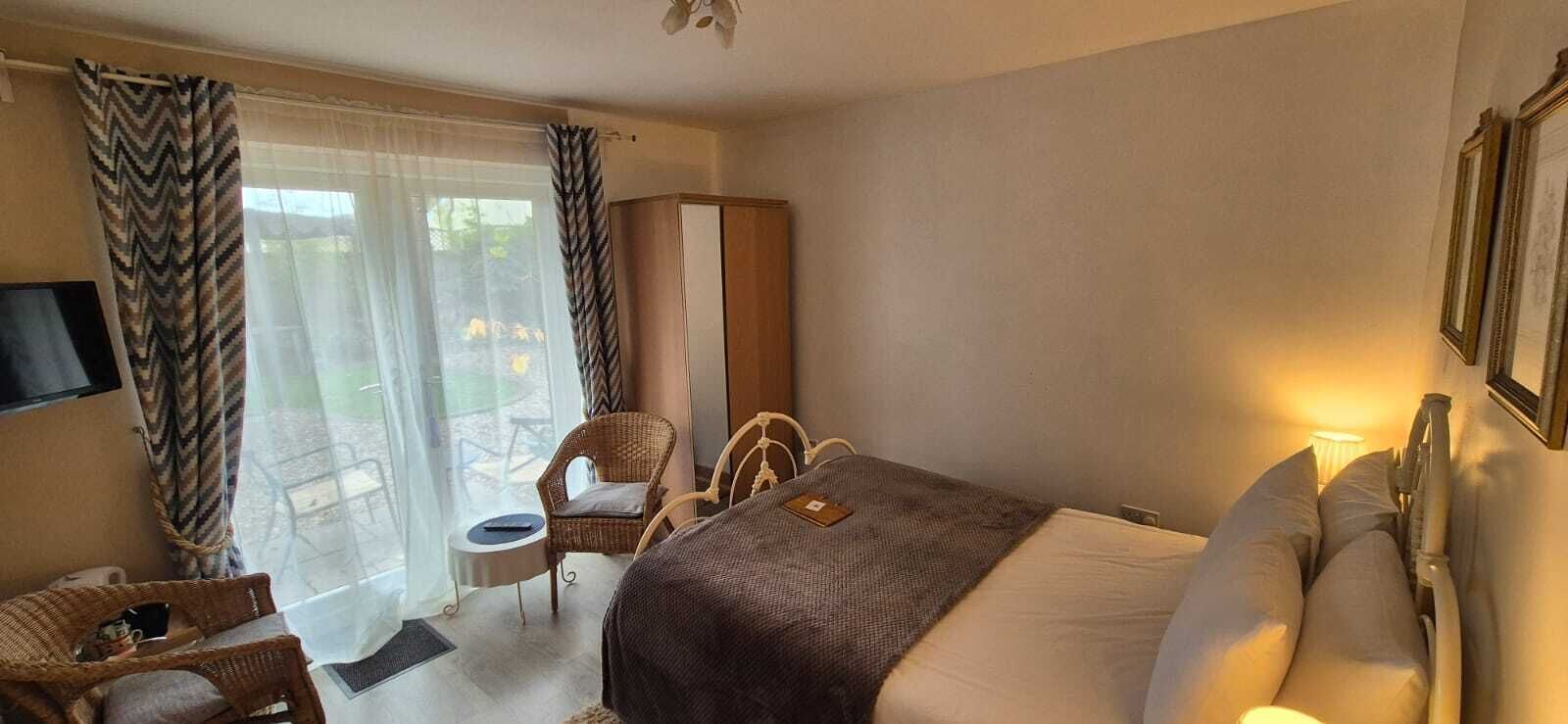 A hotel room with a bed, a chair, a small table, a TV, and a view of the outside.