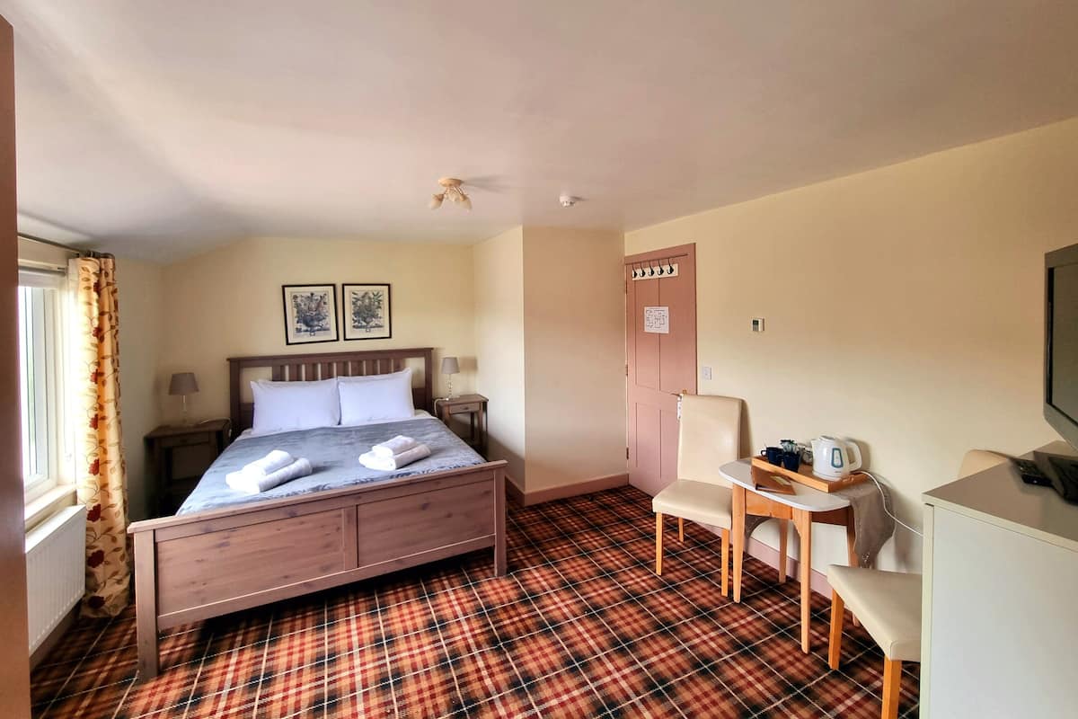 A hotel room with a bed, a desk, a chair, a radiator, and a door.
