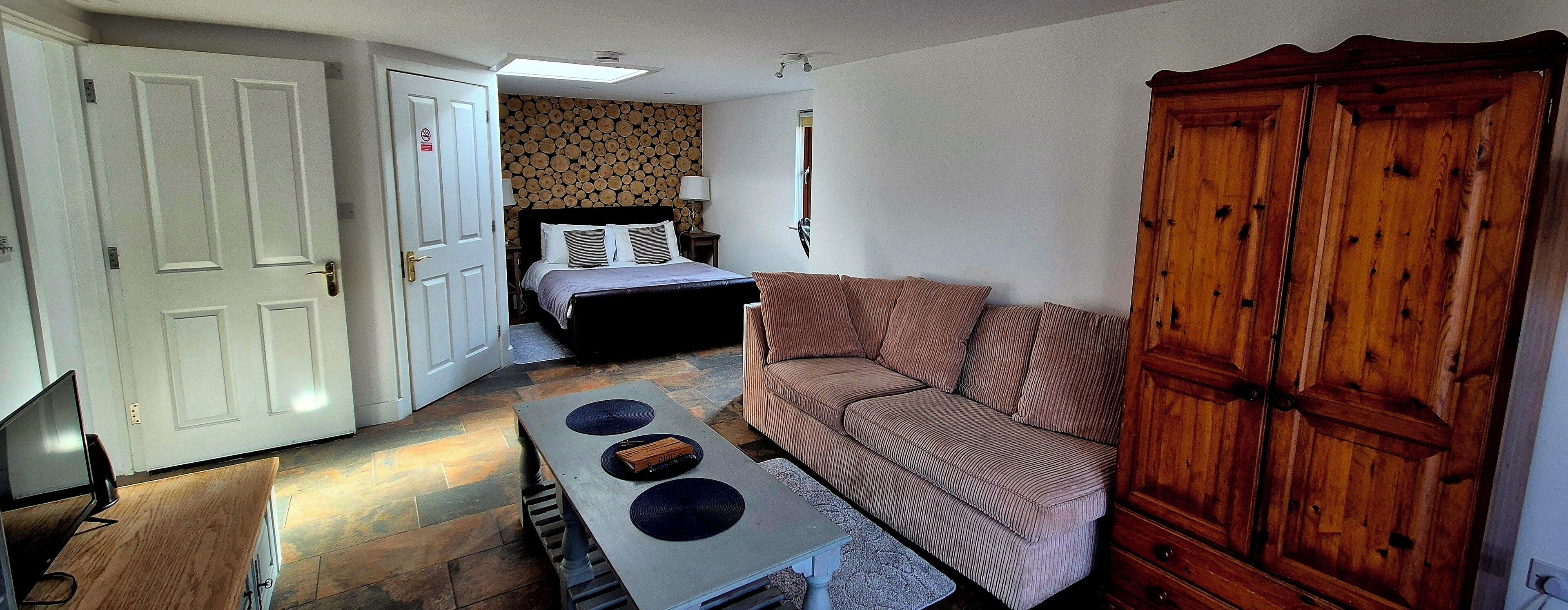 A compact hotel room with a bed, a sofa, a wooden wardrobe, and a small table with two bowls.
