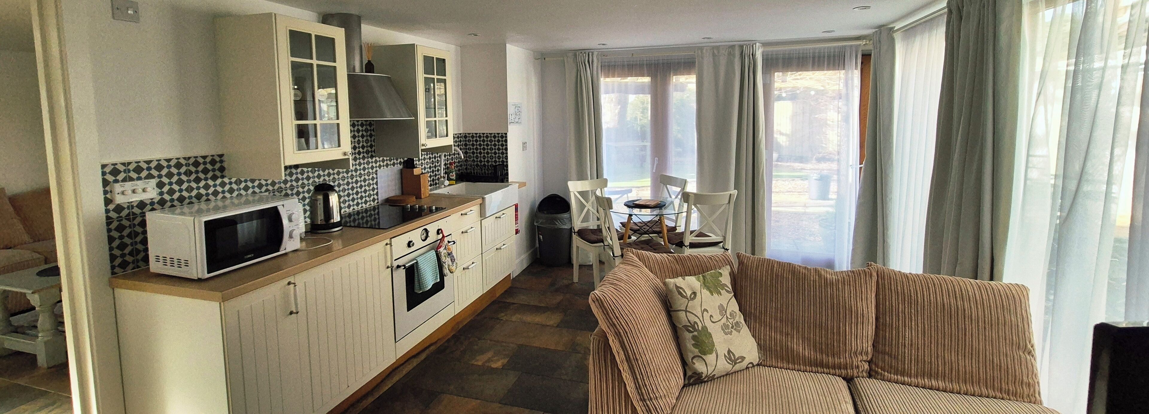 A compact kitchen with a microwave, stove, and cabinets. There is a dining area with a table and chairs, and a sofa with a cushion.