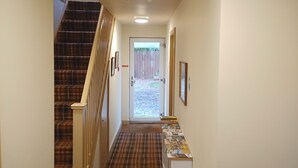 Ein Flur mit einer Treppe links, einer Tür am Ende und einem kleinen Tisch mit Gegenständen rechts.