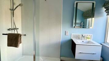 Un baño moderno con ducha de vidrio, tocador blanco con espejo y una toalla marrón en el suelo.
