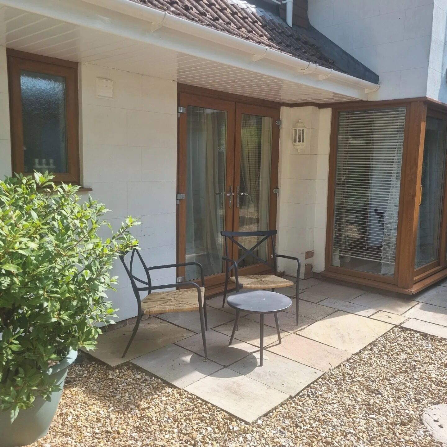 Une terrasse avec deux chaises et une table, une plante en pot et une porte-fenêtre coulissante.