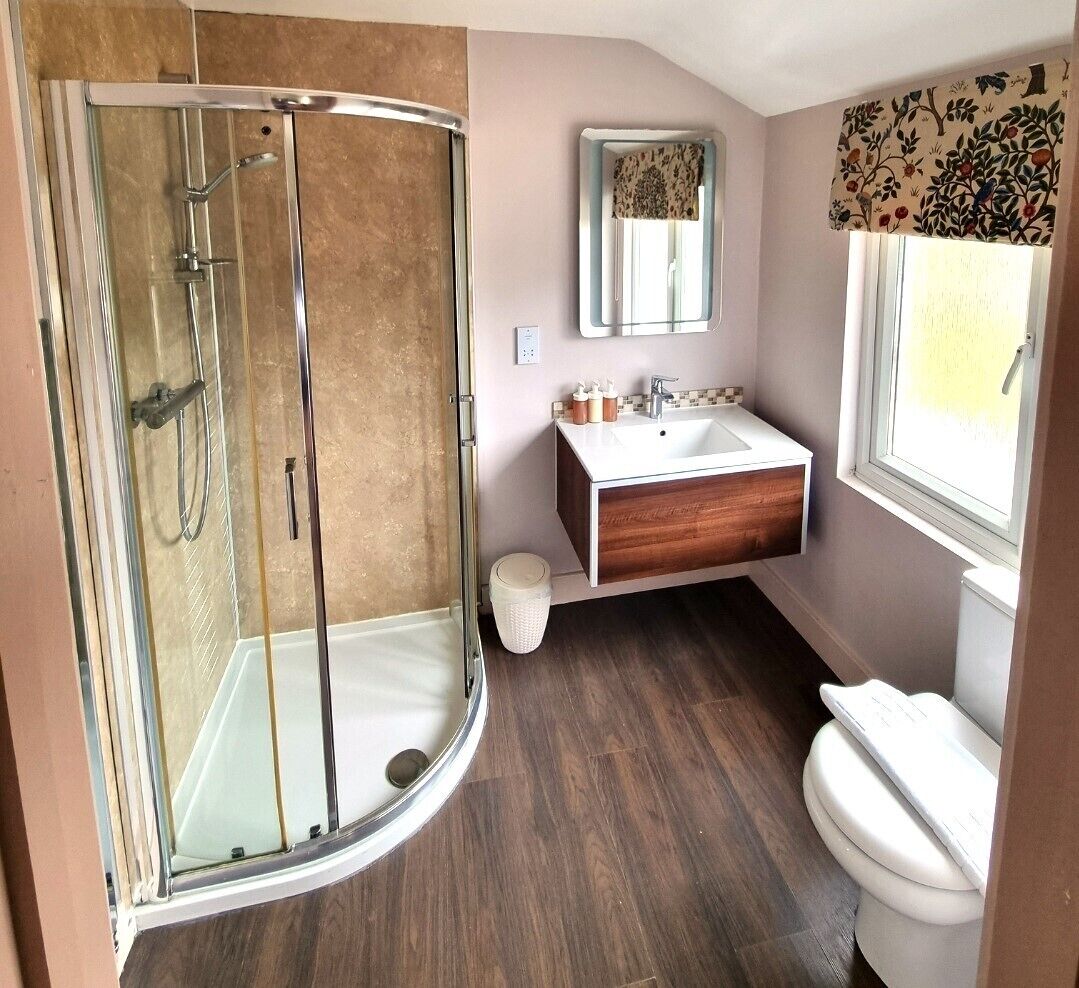 Un baño moderno con ducha envuelta en vidrio, tocador de madera y inodoro blanco.