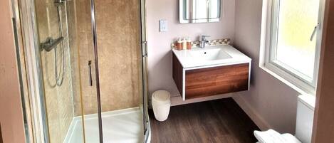 Un baño moderno con ducha envuelta en vidrio, tocador de madera y inodoro blanco.