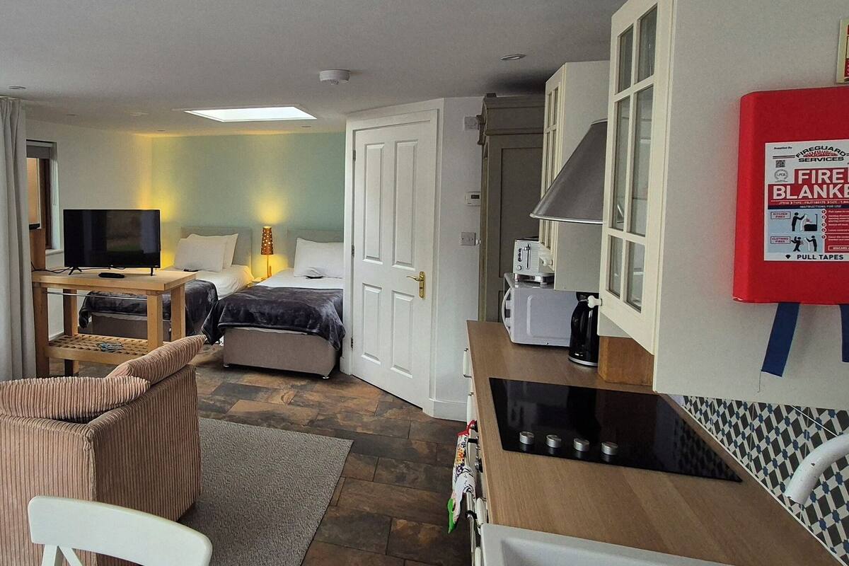 A compact hotel room with a sofa, a small dining table, a TV, and a kitchenette.