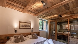 A wooden ceiling, a bed with pillows, a framed picture, and a bathroom with a mirror.