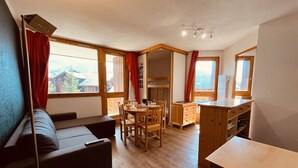 Kodikas huone, jossa on sohva, ruokapöytä ja tuolit, puulattiat ja suuret ikkunat.