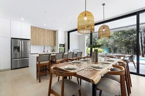 A modern kitchen with stainless steel appliances, a dining area with wooden chairs and a large table, and a view of a swimming pool through large windows.