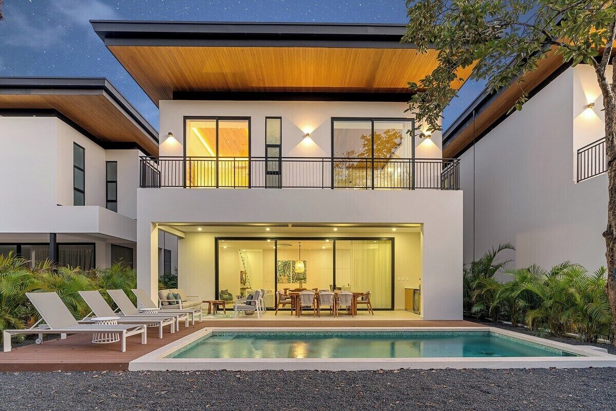 Une maison moderne à deux étages dotée d’une piscine, d’un espace salon extérieur et d’un balcon.