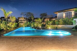 A swimming pool with a night sky view, surrounded by modern houses and tropical plants. - Villa Tropical Dawn (Bosques de Pinilla 10, Hacienda Pinilla)