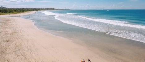 Una playa con cielo despejado, olas suaves y algunas personas caminando por la orilla.