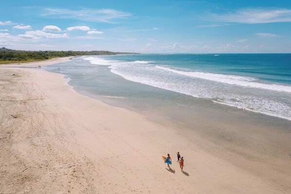 A beach with a clear sky, gentle waves, and a few people walking along the shore.